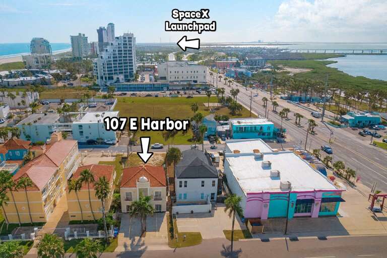 Aerial View Of Coastal Buildings, Palm-lined Streets, And Distant SpaceX Launchpad