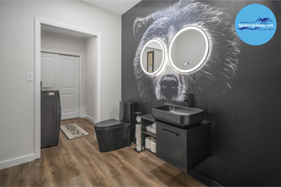 Bathroom With Raccoon Mural, Round Mirrors, Black Fixtures, Wood Flooring