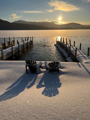 Sunlit Snowy Scene With Serene Lake, Shadowed Chairs, And Distant Mountains