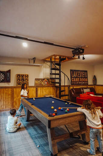 Children Playing Pool In A Rustic Game Room With A Spiral Staircase