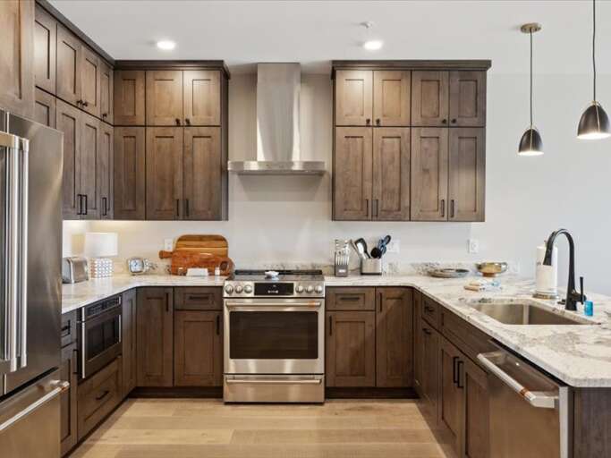 Spacious Kitchen With Stainless Steel, Sleek Surfaces, And Hanging Pendant Lights