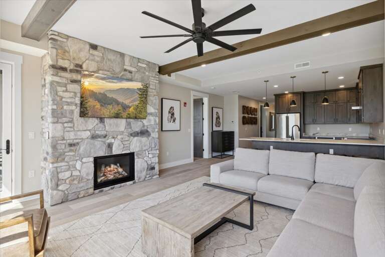 Spacious Living Space With Stone Fireplace And Sectional Sofa, Sleek Kitchen In Background Spacious Living Space With Stone Fireplace And Sectional Sofa, Sleek Kitchen In Background