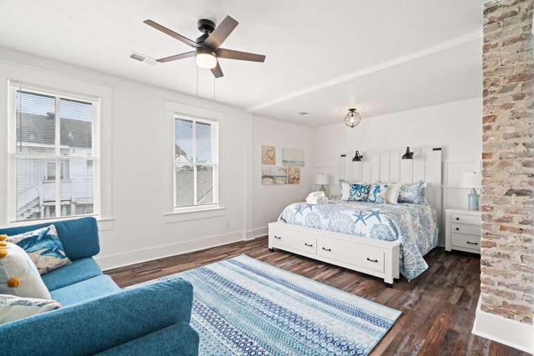 Bright Bedroom With Blue Bedding, Brick Wall, Wooden Floor, Fan Overhead
