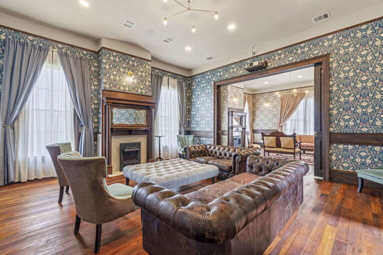 Elegant vintage-style living room with rich wood floors, classic fireplace, and plush leather seating, perfect for cozy, stylish gatherings.