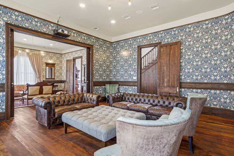 Spacious, vintage-inspired living room with rich textures, classic leather seating, and elegant wallpaper for timeless comfort.