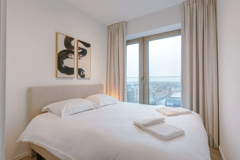 Bedroom With Large Bed, White Linens, Cityscape View Through Window, Wall Art Hanging