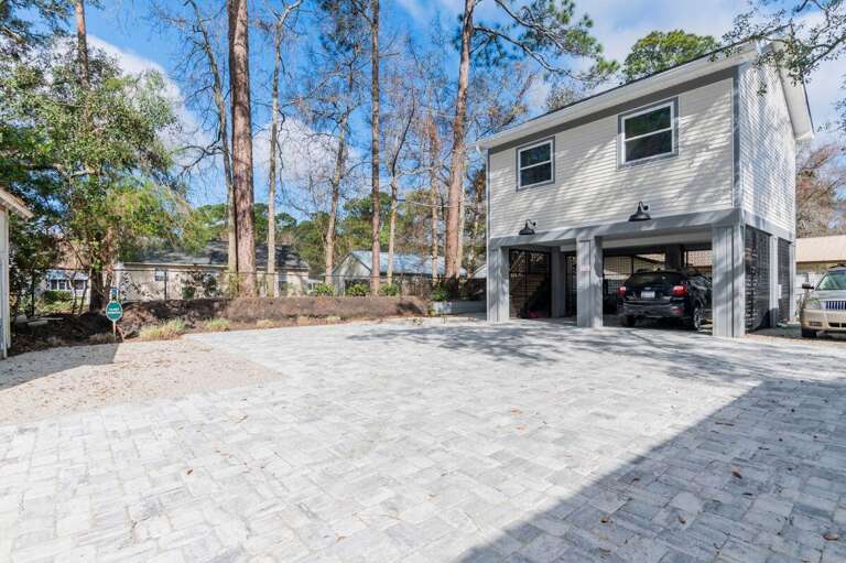 Two-story Building With Open Garage And Paved Driveway, Surrounded By Tall Trees