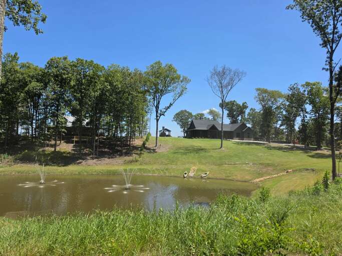 Peaceful pond with fountains, kayaks, and a picturesque view of the cabin and surrounding property.
