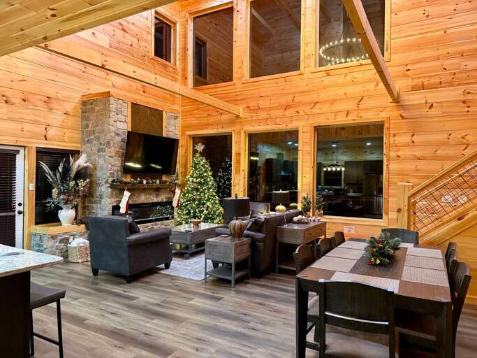 Wood-paneled Living Space With Stone Fireplace, Large Windows, And Dining Area