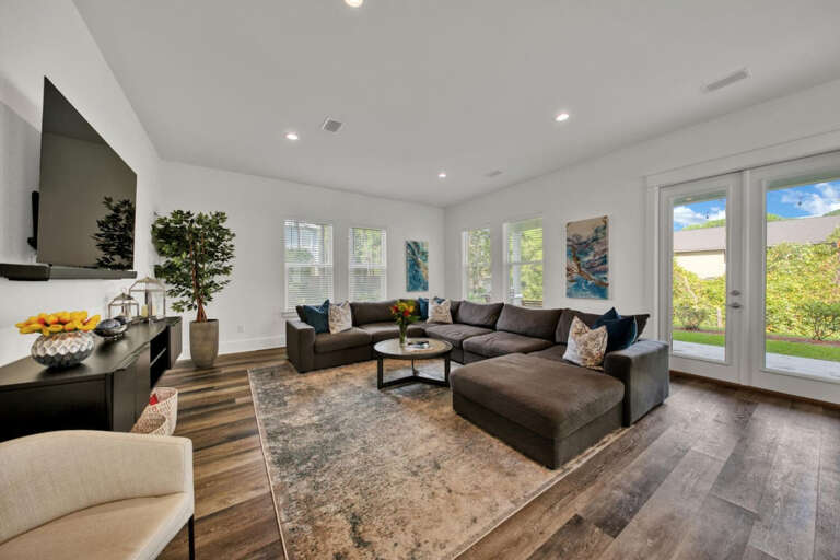 Spacious Living Room With Sectional Sofa, Sleek Surfaces, And Sunlight Streaming Through Large Windows