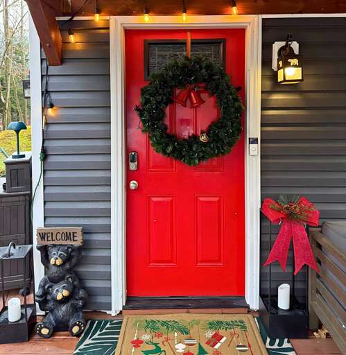 Red Door Decorated With Holiday Wreath, Wooden Bear Statue, And Welcoming Mat