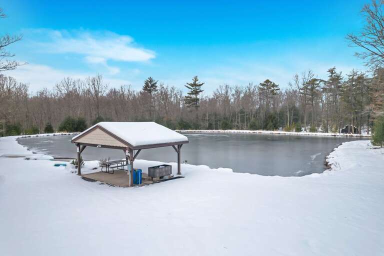 Pavilion On Partially Frozen Pond In Snowy Setting With Trees
