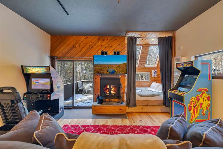 Wood-walled Room With Arcade Games, Sofa, And Stove; Snowy View Through Glass Door