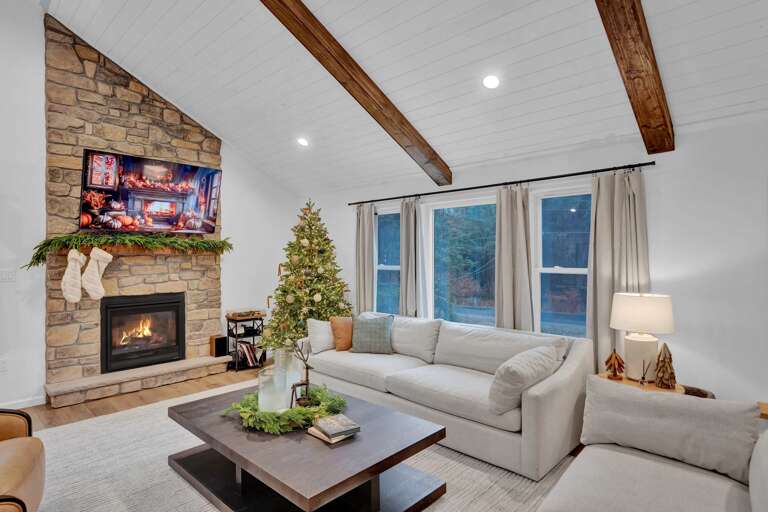 Stone-stacked Fireplace Flanked By Festively Fir-trimmed Windows In A Lush Living Room