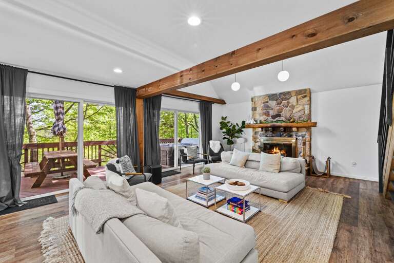 Spacious Living Space With Stone Fireplace, Wooden Beams, And Balcony View