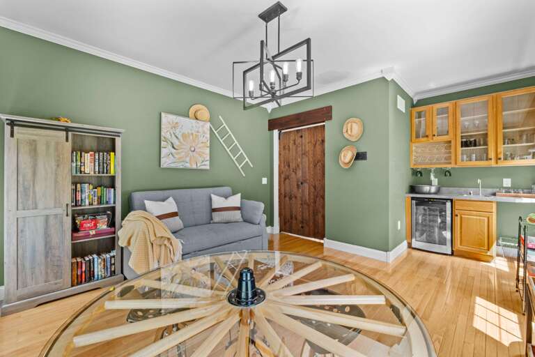 Green-walled Room With Wooden Bookshelf Beside Sofa, Star-shaped Coffee Table Center, And Kitchen In Rear