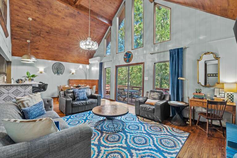 Spacious Living Room In A Vacation Rental With High Ceilings And Large Windows, Featuring Wood Paneling And Blue Decorative Accents