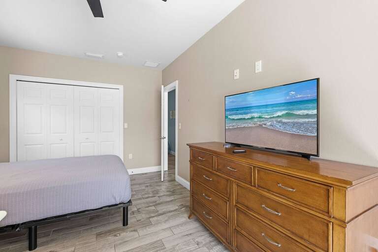 Relax in this comfortable bedroom featuring a cozy bed, dresser, and flat-screen TV. Perfect for your beach stay, unwind with your favorite shows after a fun day soaking up the sun and ocean breeze.