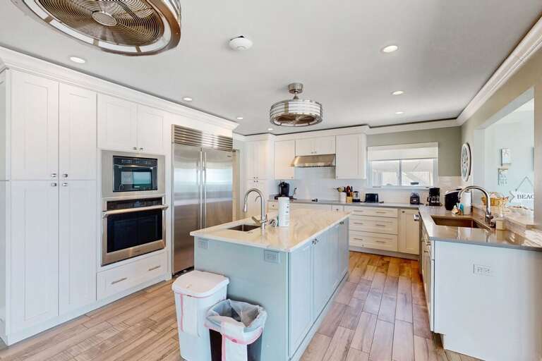 Cook with ocean breezes nearby in this bright, beach-style kitchen featuring stainless appliances, a large island, and plenty of space for family meals during your beach stay.