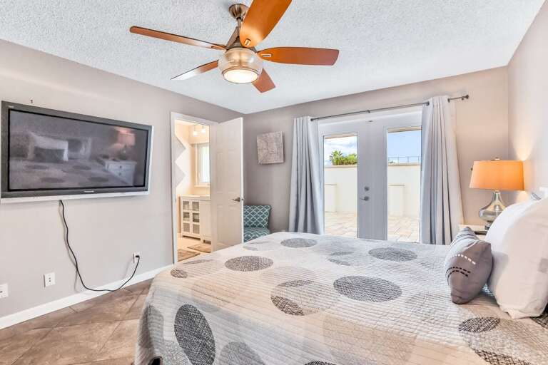 Enjoy a relaxing beach stay in this sunny bedroom featuring a comfy bed, large TV, private bath access, and French doors leading to the outdoor patio—perfect for unwinding after a day by the ocean.
