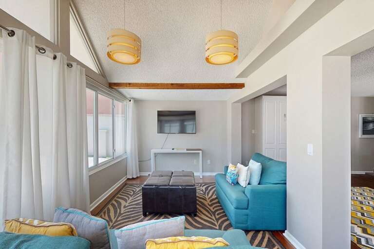 Enjoy this sunny beach stay lounge featuring vibrant seating, large windows, and a flat-screen TV—perfect for relaxing after a day on the sand and surf.