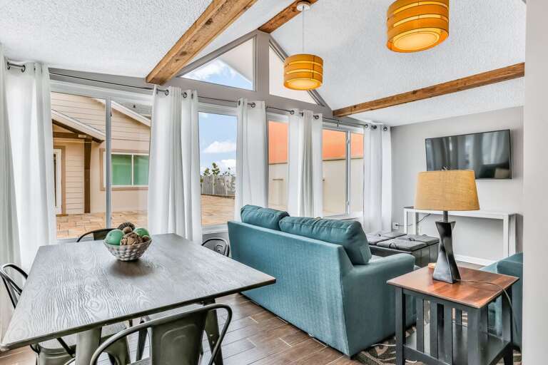 Relax in this airy beach stay living area featuring vaulted ceilings, modern décor, and large windows that open to the sunny patio. Perfect for gathering after a day on the sand and surf.