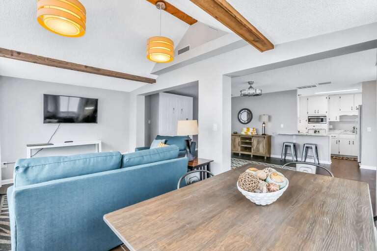 Relax in this airy beach stay living and dining area featuring cozy seating, coastal décor, and easy flow to the kitchen—perfect for gathering after a day on the shore.
