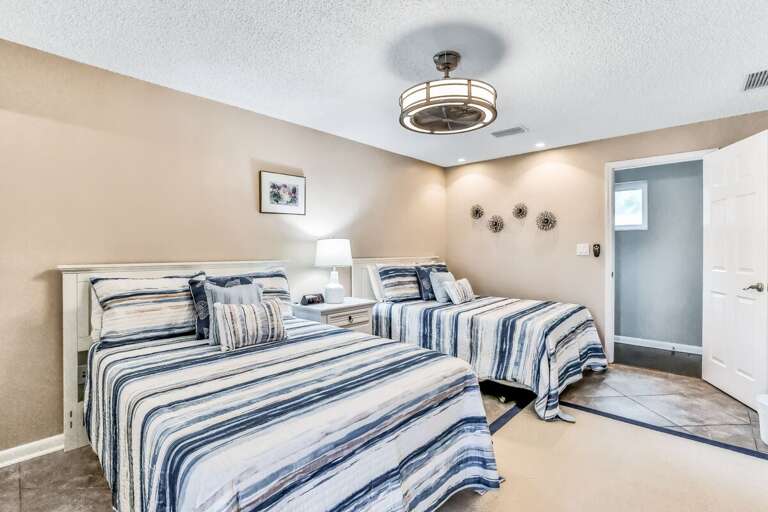 Relax in this inviting beach stay bedroom featuring two comfy beds, coastal bedding, soft lighting, and easy access to the ensuite bath—perfect for unwinding after a day on the sand.