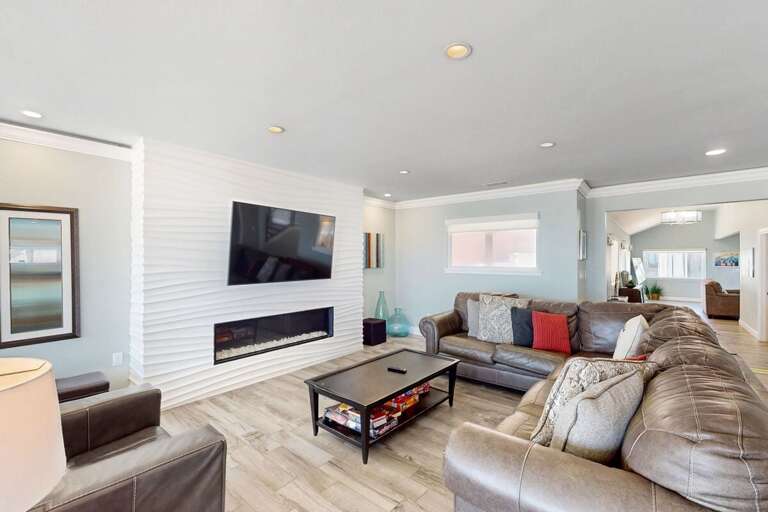 Relax in this stylish beach-stay living room featuring a sleek fireplace, plush leather seating, and plenty of space to unwind after a day on the sand and surf. Perfect for cozy coastal nights.