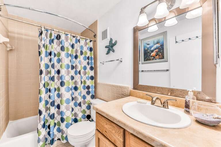 A bright, beach-inspired bathroom featuring a colorful shower curtain, spacious vanity, and coastal décor—perfect for refreshing after a day of sun and surf during your beach stay.