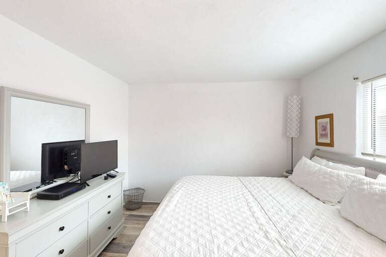 Relax in this airy beachside bedroom featuring a plush king bed, soft natural light, and simple coastal décor—perfect for unwinding after sun-filled days on the shore.