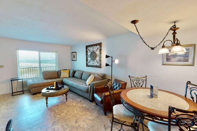 Relax in this bright beach stay living space featuring a plush sectional, stylish décor, and an inviting dining area—perfect for unwinding after a sun-soaked day by the ocean.