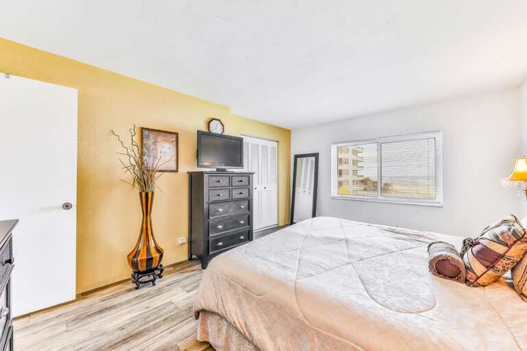 A spacious beach stay bedroom featuring a plush king bed, warm accent wall, natural light, and plenty of storage—perfect for relaxing after a sun-soaked day by the ocean.