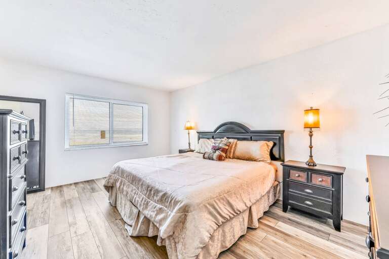 Spacious, sunlit bedroom with a plush king bed and warm lighting—perfect for unwinding after a day of beachside fun during your coastal stay.