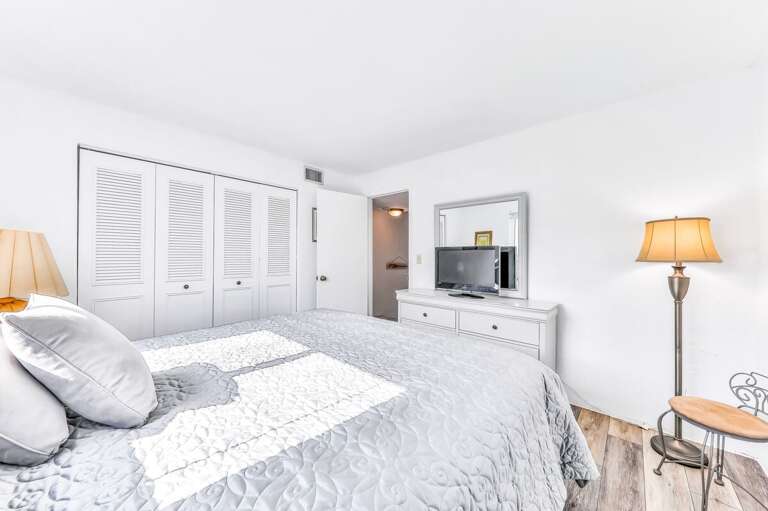 Sunny beach stay bedroom with a comfy bed, crisp white décor, and plenty of storage—perfect for unwinding after a day on the sand and surf.