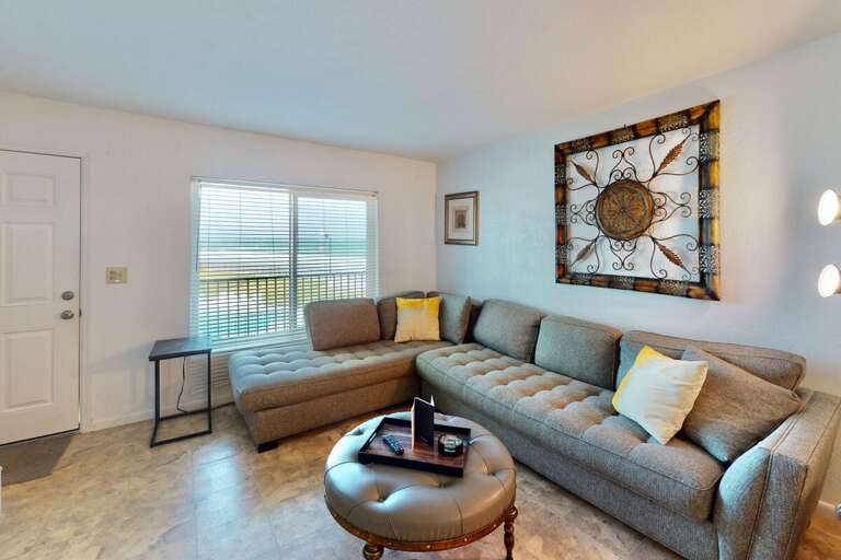 Unwind after your beach adventures in this cozy living room featuring a spacious sectional, warm natural light, and inviting coastal décor—perfect for relaxing during your seaside stay.
