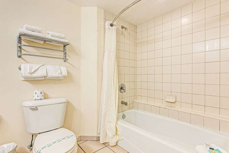 Bathroom With Beige Tiles, Bathtub, Toilet, And Towel Rack