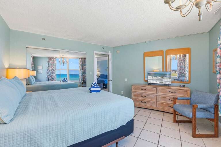 Relax in this spacious oceanfront king bedroom featuring coastal décor, a dresser with TV, mirrored