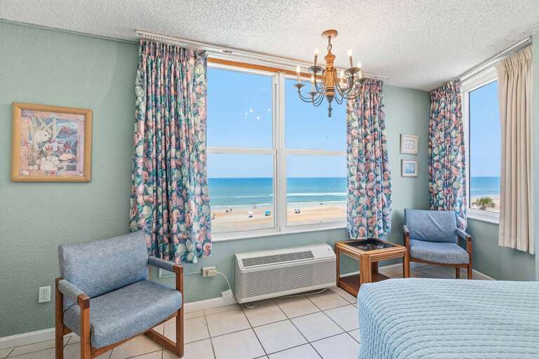 Wake up to sweeping ocean views from this bright beachfront bedroom featuring large windows, cozy