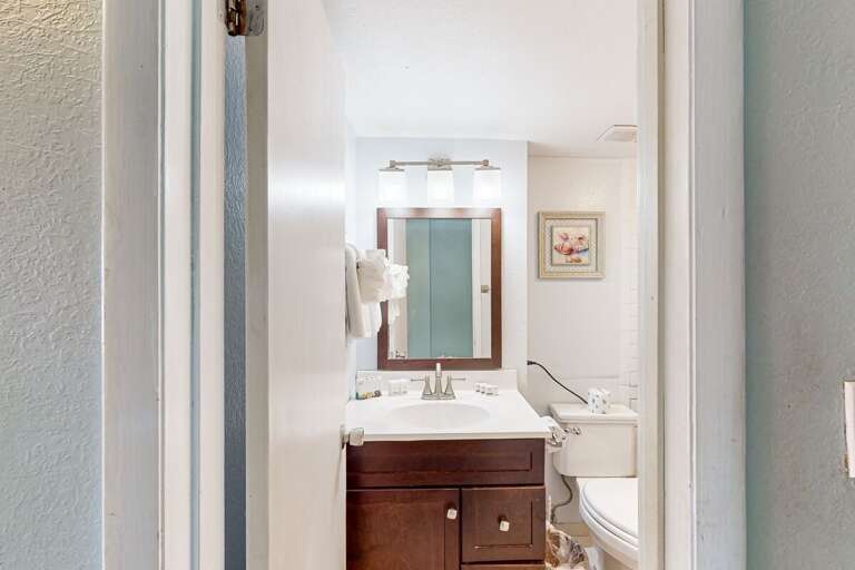View Into A Bathroom With A Mirror And Sink Flanked By Frames