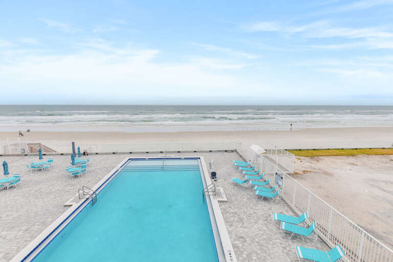 Seaside Scene With Pool, Pristine Beach, And Pale Blue Chairs