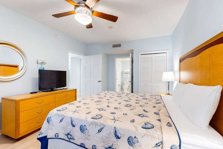 Bright beach-inspired bedroom featuring a comfy bed with seashell décor, private bathroom access, and plenty of space to unwind after a sun-soaked beach stay.