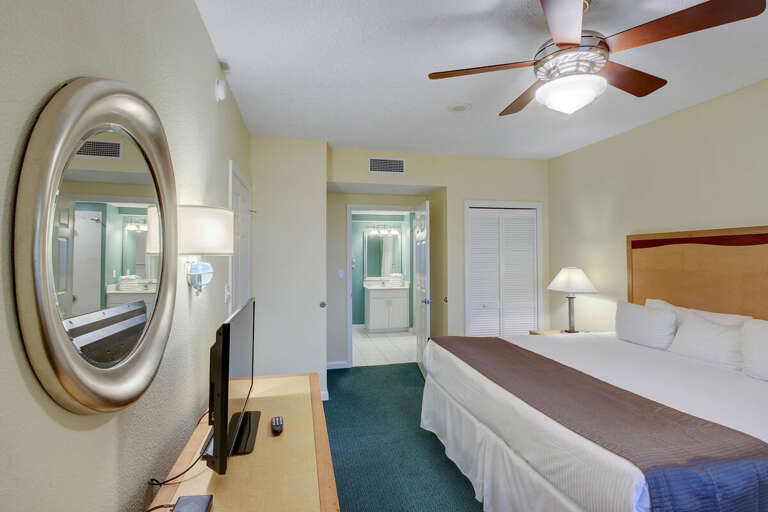 Spacious beach-style king bedroom with cozy lighting, a large bed, and direct access to a bright en-suite bathroom—perfect for unwinding after relaxing days by the ocean.