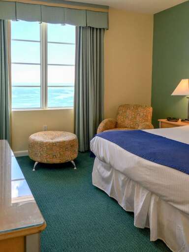 Sunny beach-style bedroom with ocean views, cozy seating, and fresh coastal bedding—an inviting retreat to unwind after a relaxing day by the shore.