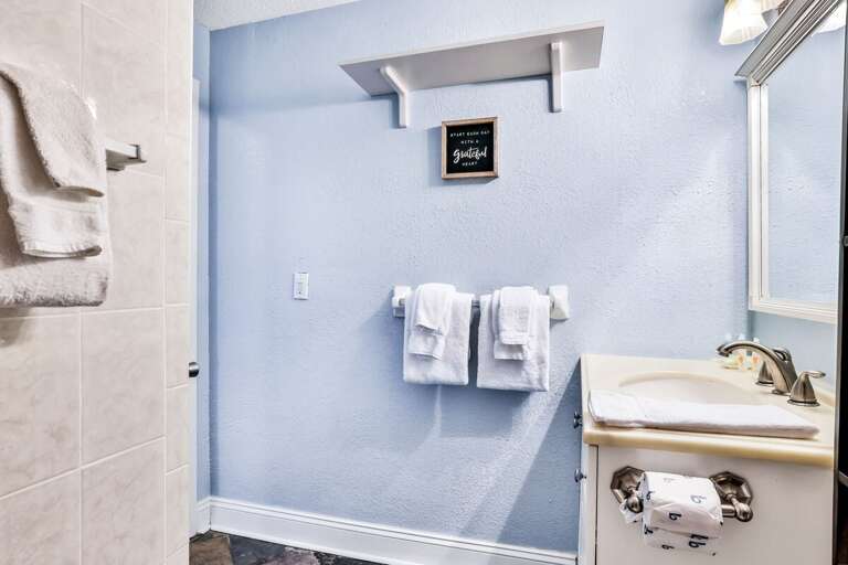 Blue Bathroom With Bright Shelves, Beige Basin, And A Shower Space