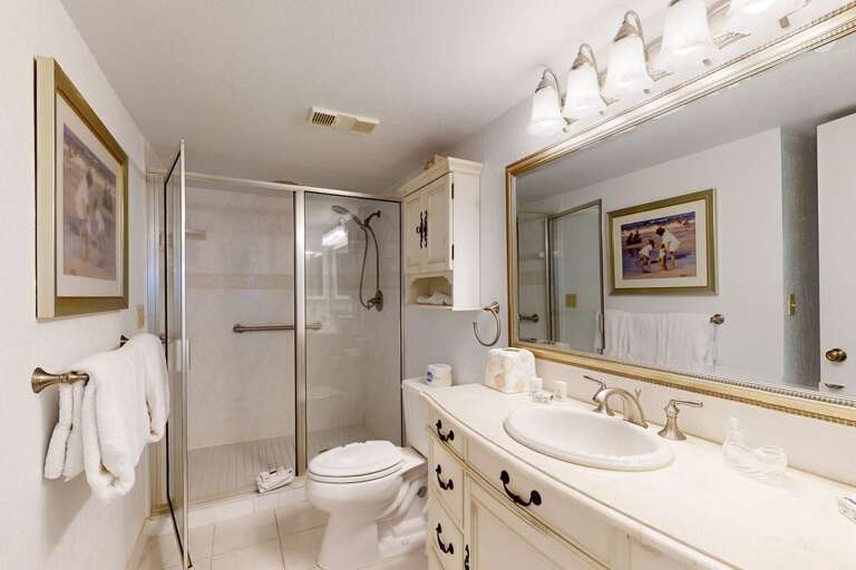 Enjoy a clean, roomy bathroom featuring a walk-in shower, large vanity, and soft coastal décor—providing comfort and convenience throughout your relaxing beach stay.