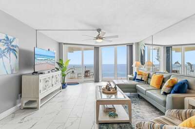 Relax in this bright oceanfront living room featuring panoramic beach views, floor-to-ceiling