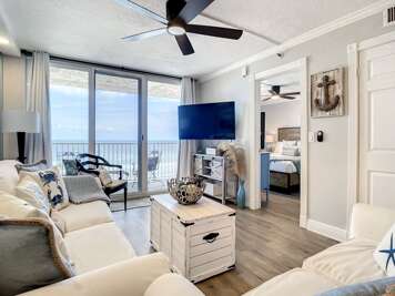 Bright living area with oceanfront balcony access, cozy seating, and a large flat-screen TV.