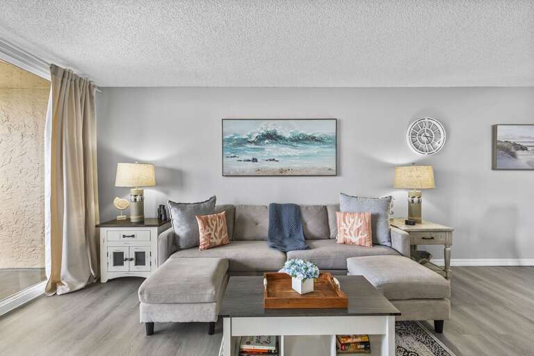 This inviting living room exudes coastal elegance, featuring a plush sectional sofa adorned with soft coral-themed pillows and a cozy throw.