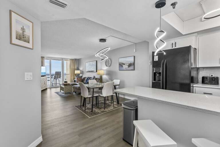 This inviting open-concept space seamlessly combines a modern kitchen, dining area, and cozy living room, all flowing towards a stunning ocean view.